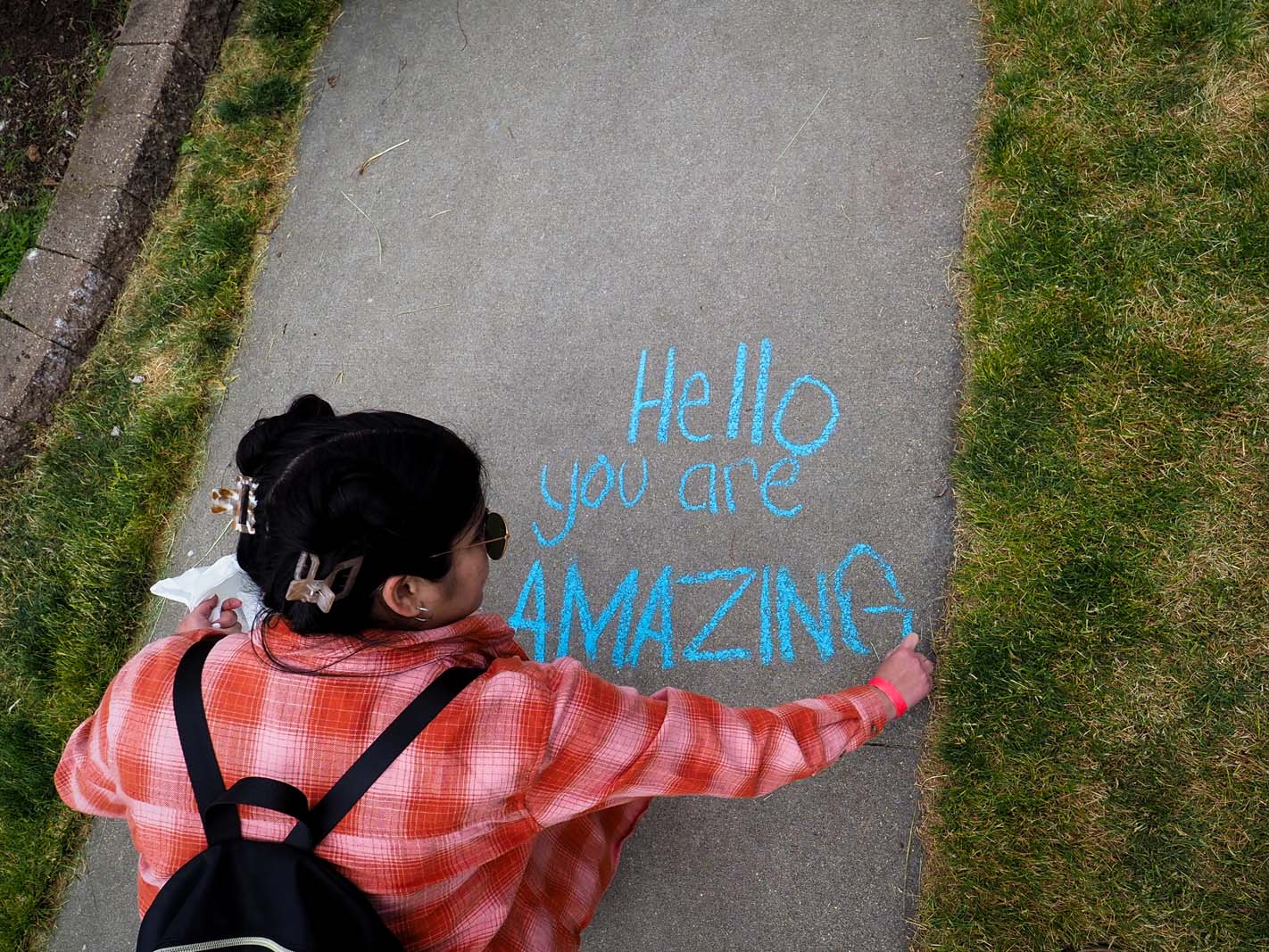 A 2023 GH Pride attendee writing "Hello, you are amazing" with sidewalk chalk.